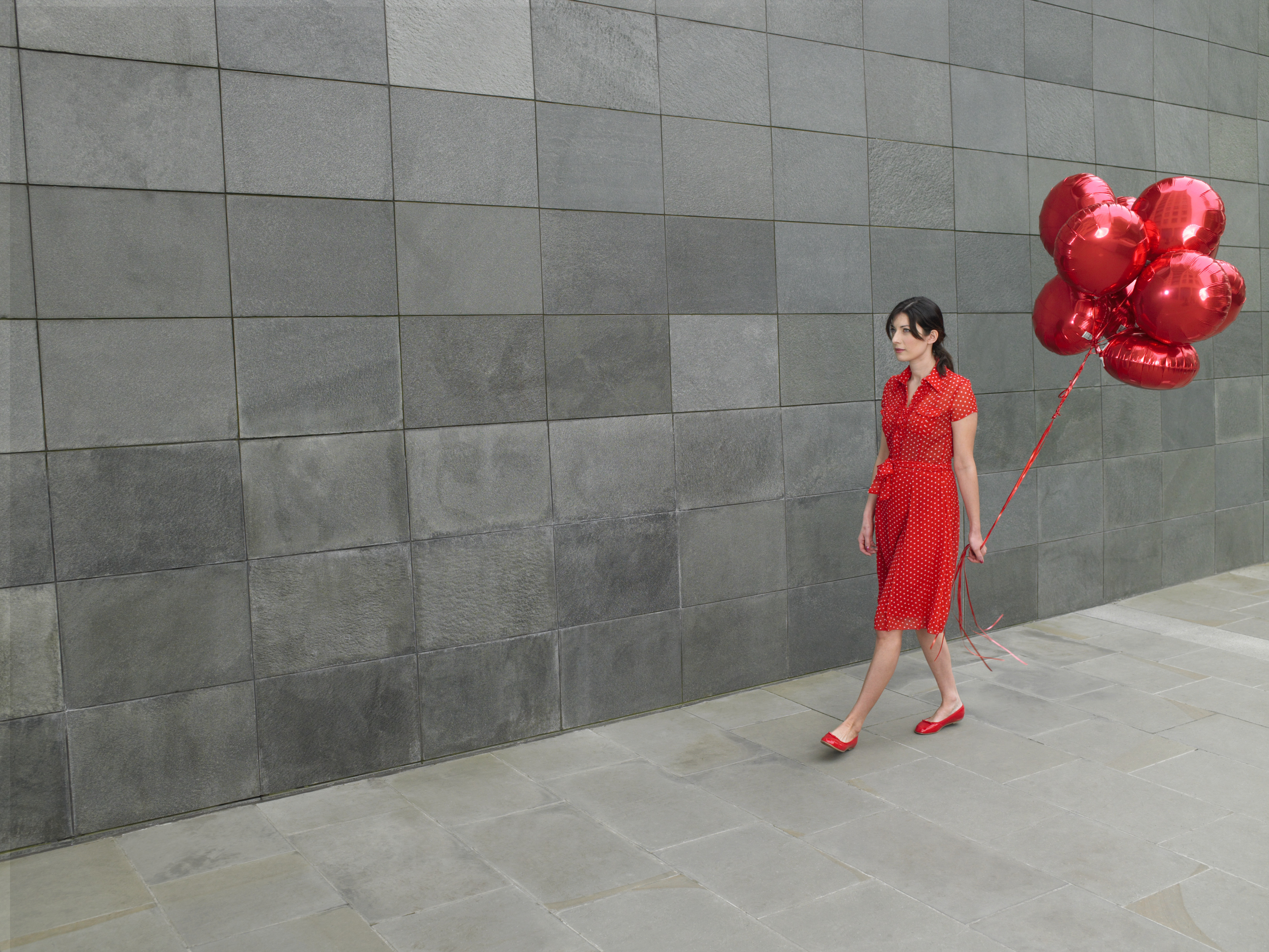 Young woman walking along holding bunch of red foil balloons