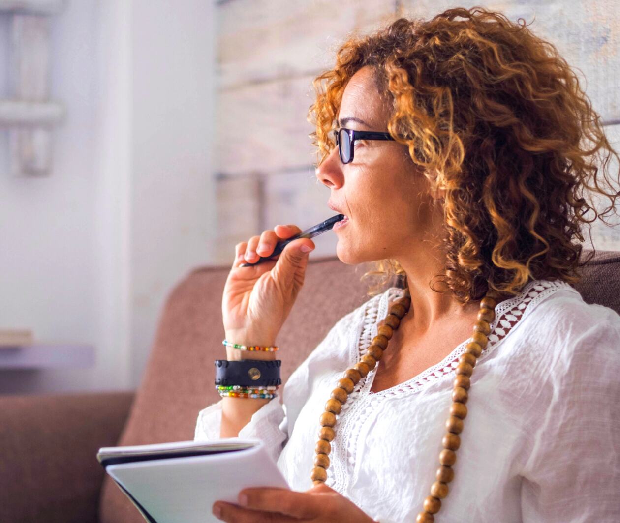 A woman seated at a desk with a pen, looking off into the distance, thinking.