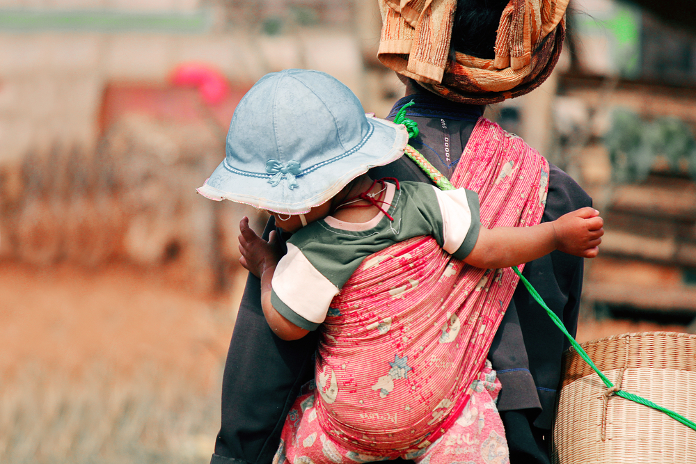 A child on the back of her mother wearing a blue hat.