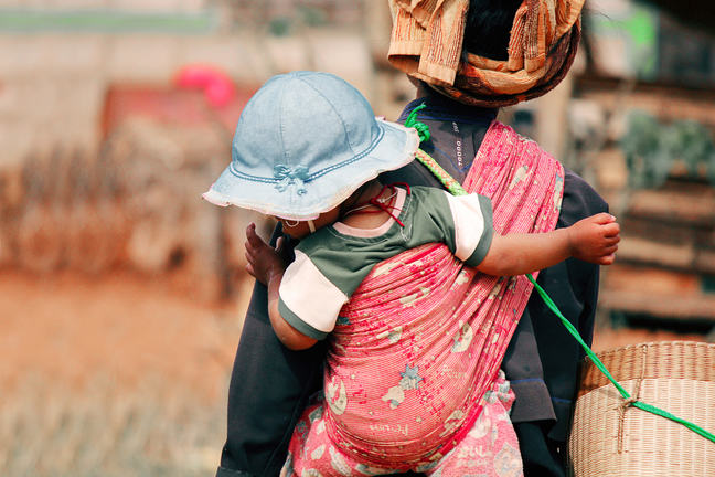 A child on the back of her mother wearing a blue hat.