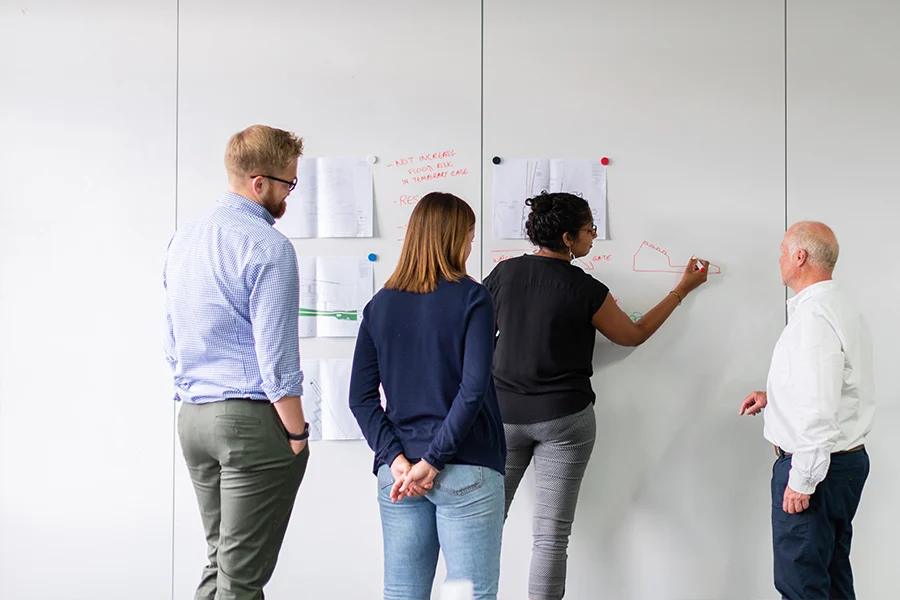 Four people standing by a whiteboard as a woman is drawing something.