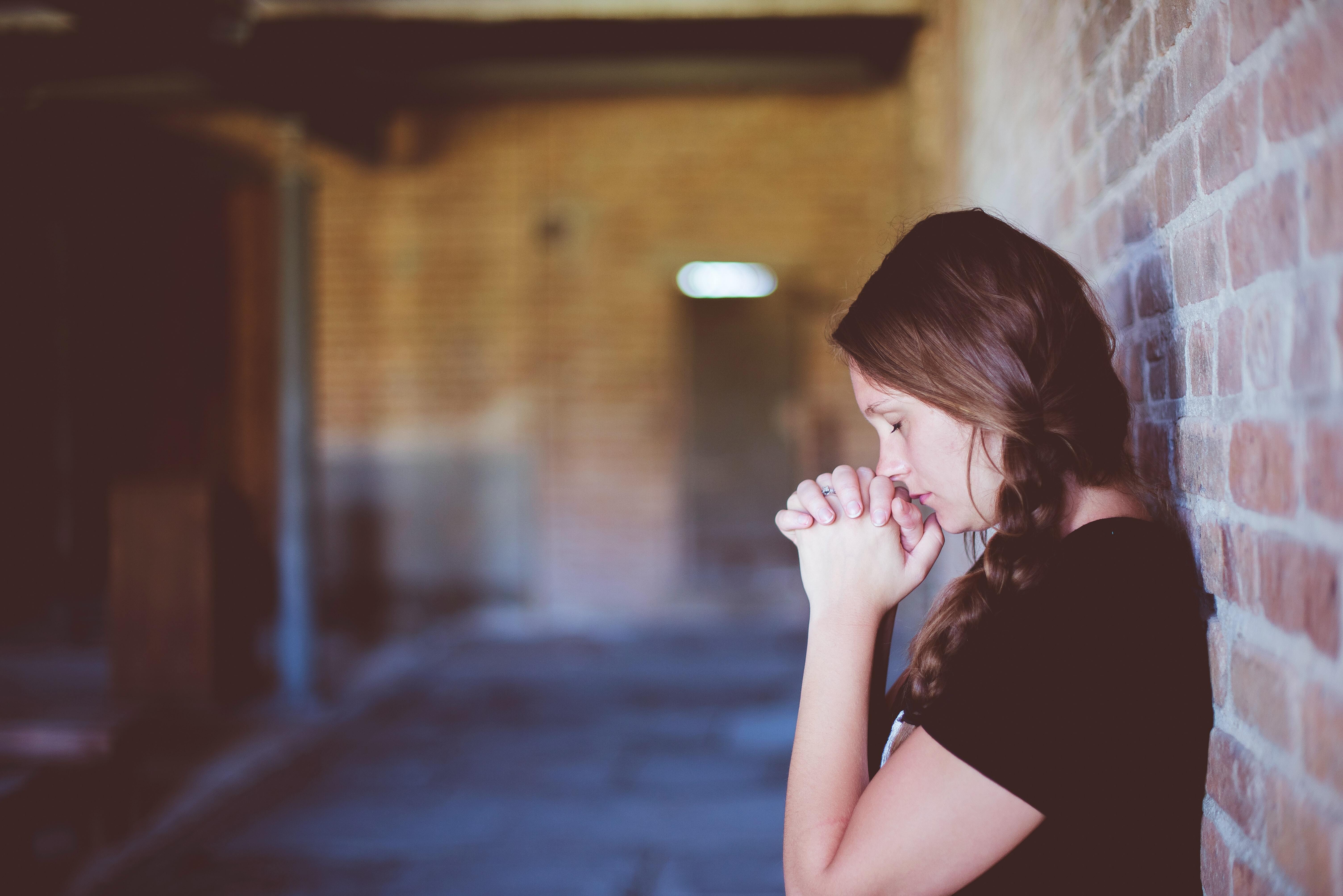 Lady leaning against a brick wall with her hands clasped