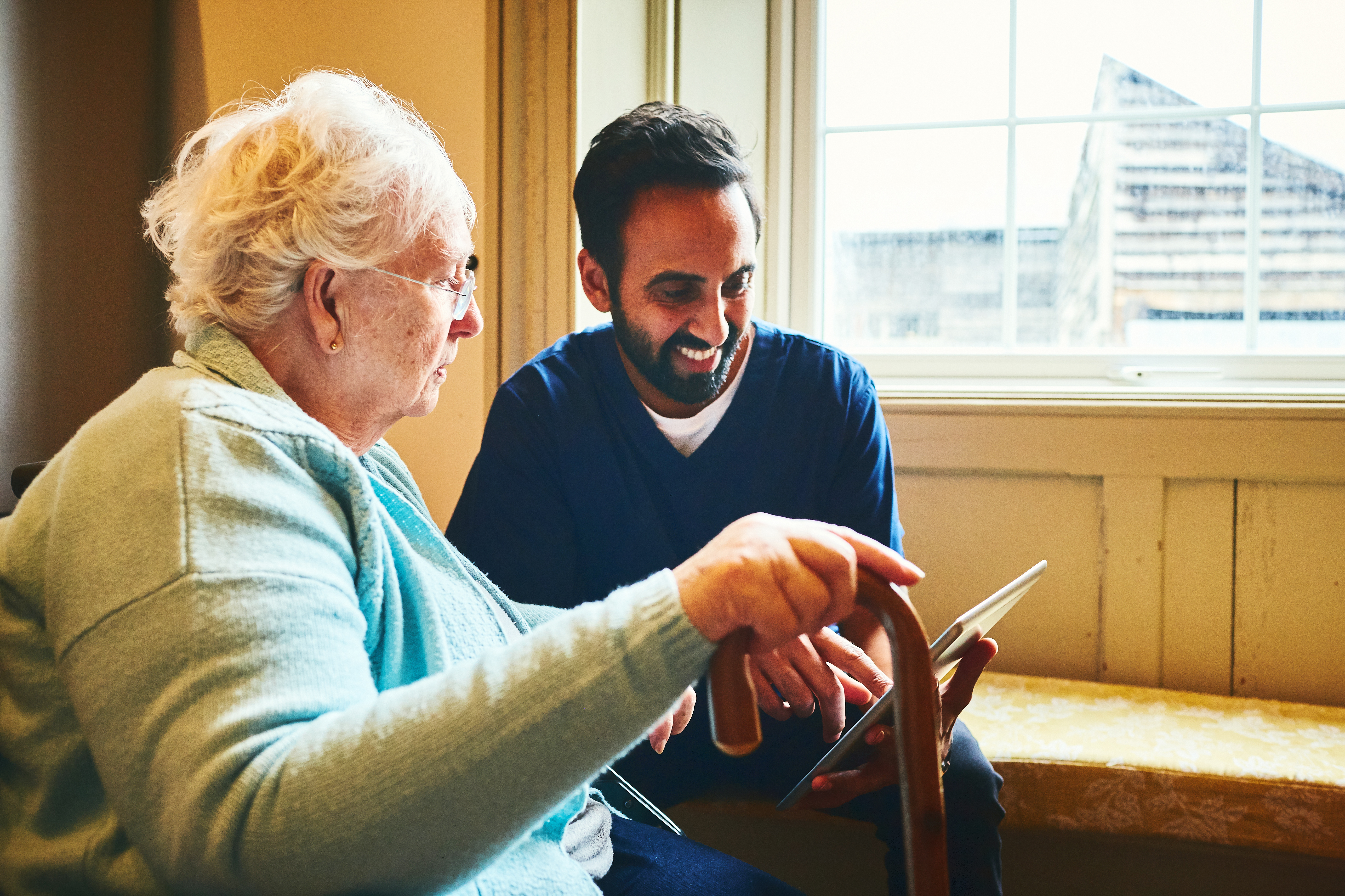 Male social care worker showing a digital tablet to an elderly woman