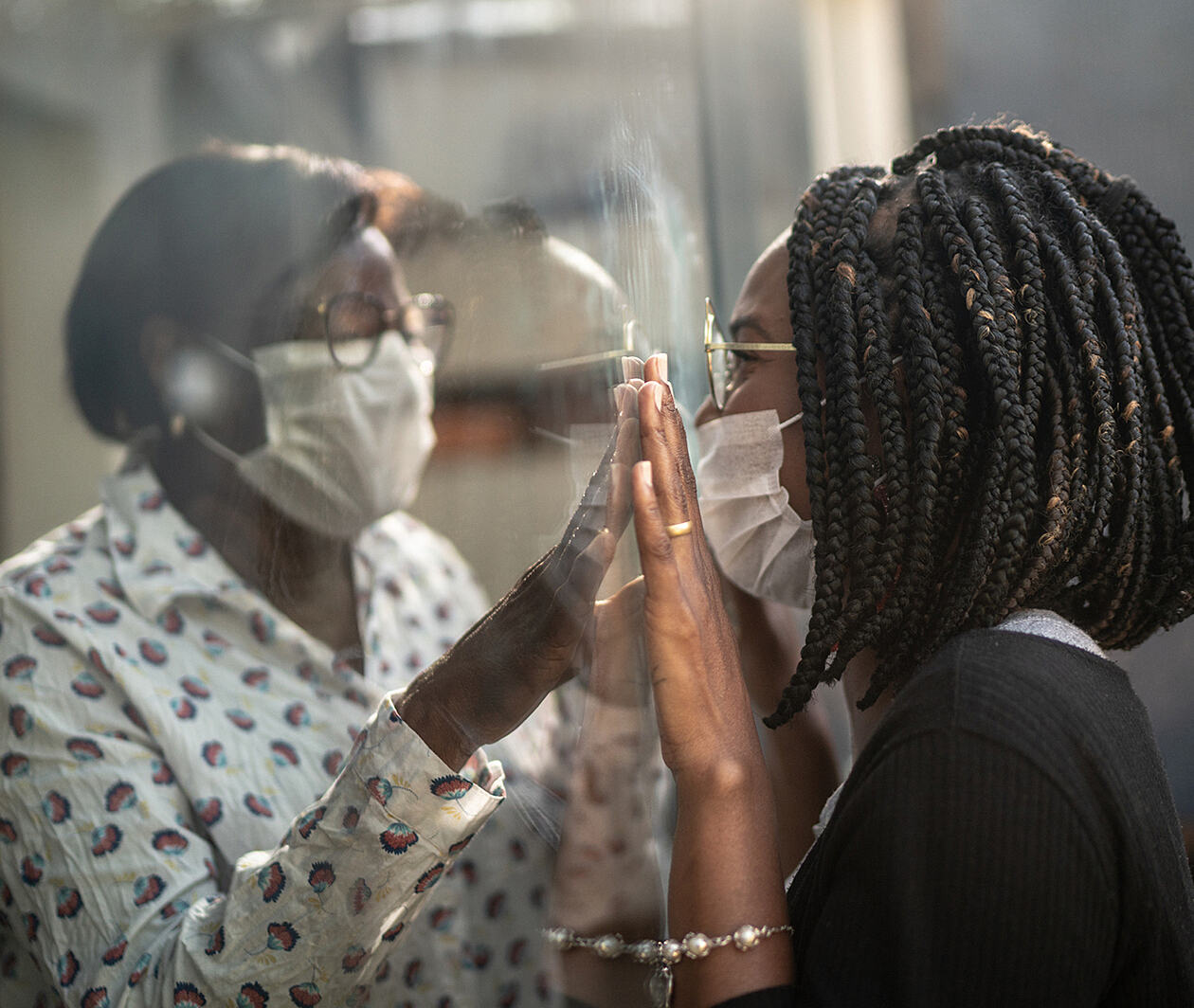 Two people either side of a clear plastic wall pressing their hands against each other.