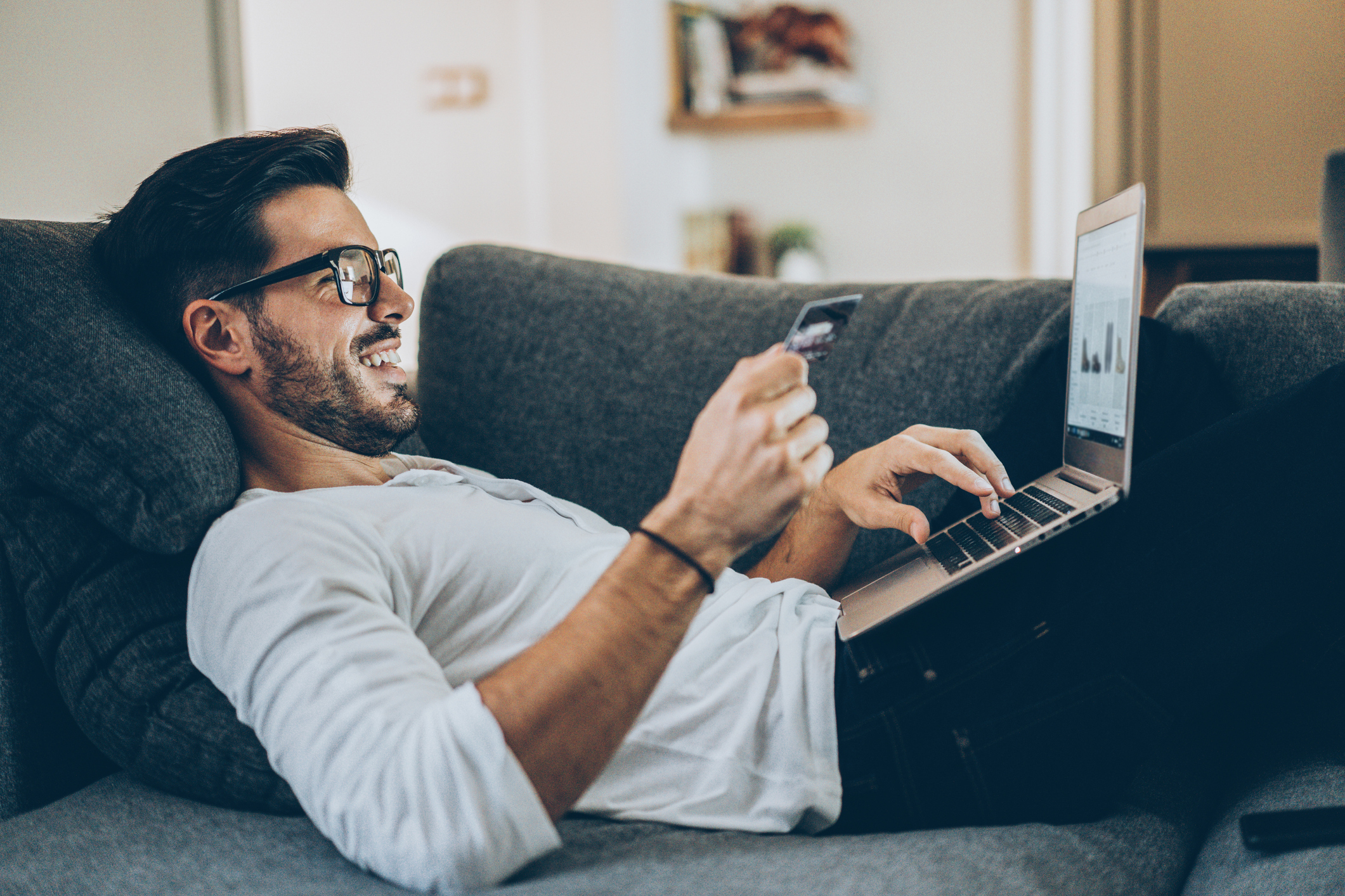 A person browsing on a sofa with their credit card, shopping online.