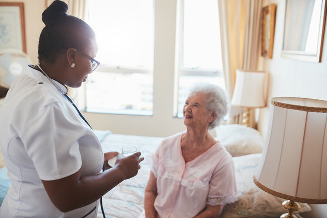 A Carer supplying a smiling resident with her medicines and a glass of water