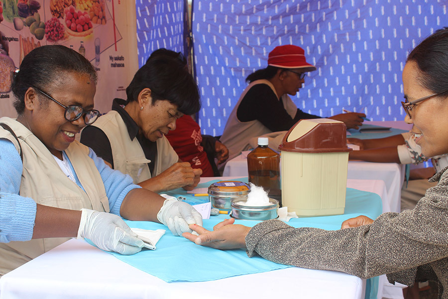 Health workers take pinpricks of blood from patients in a camp setting