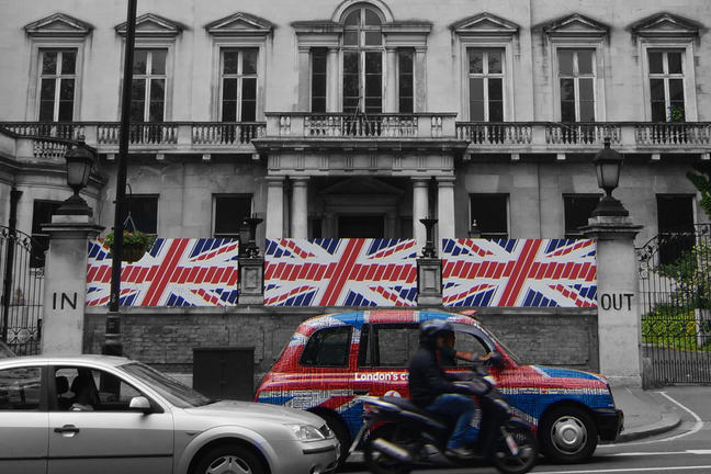 Street in London with UK flags on a wall outside a building with 'in' and 'out' signs on either side of wall
