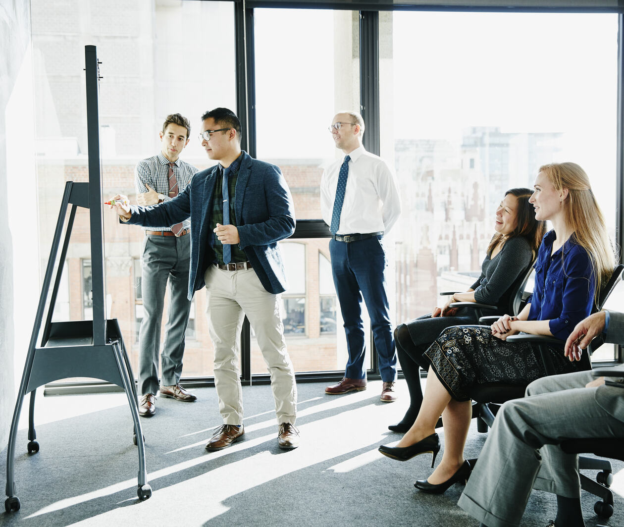 Businessman presenting ideas at whiteboard during meeting in office conference room, making leadership decision.