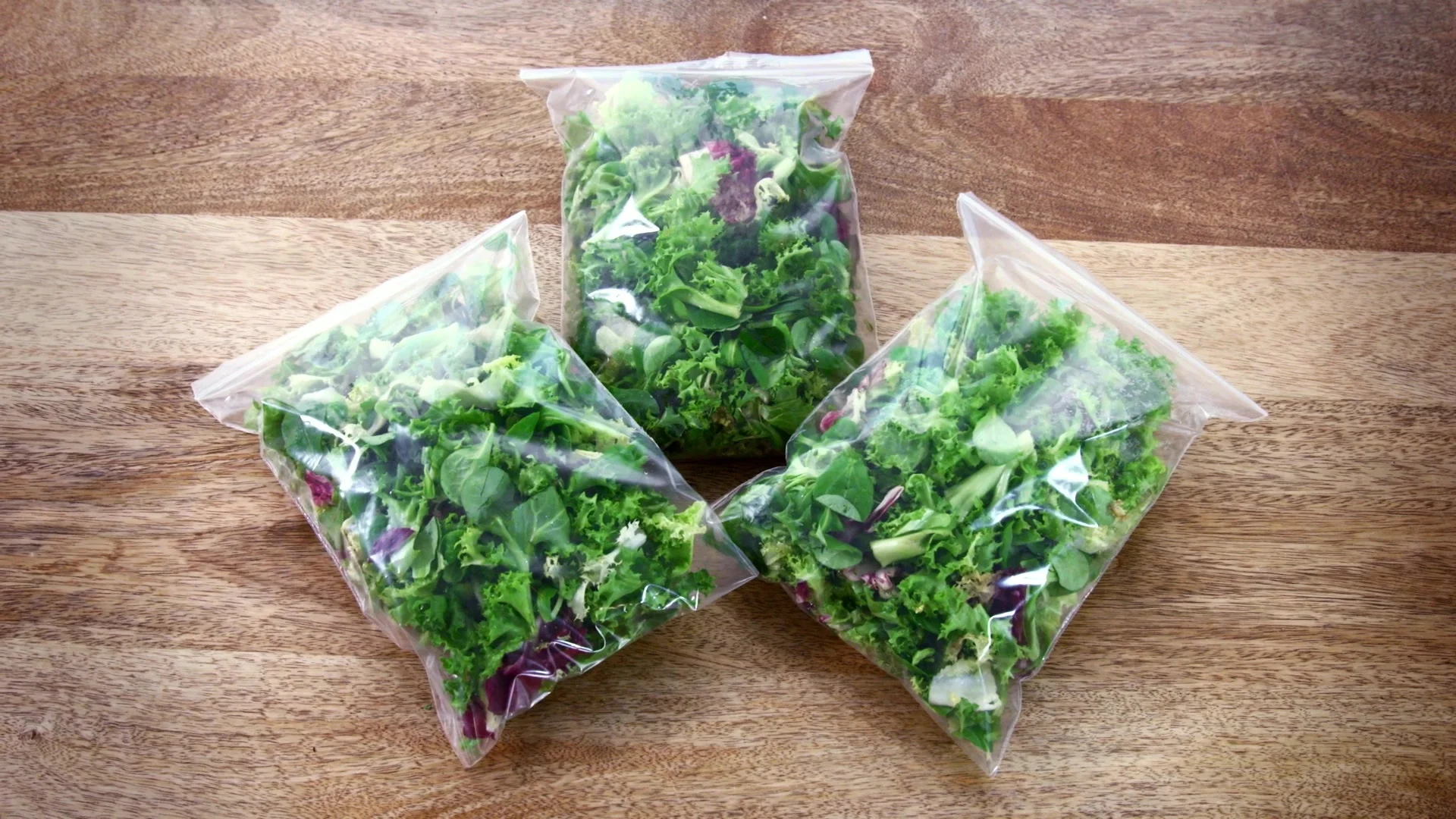 3 bags of salad on a wooden table